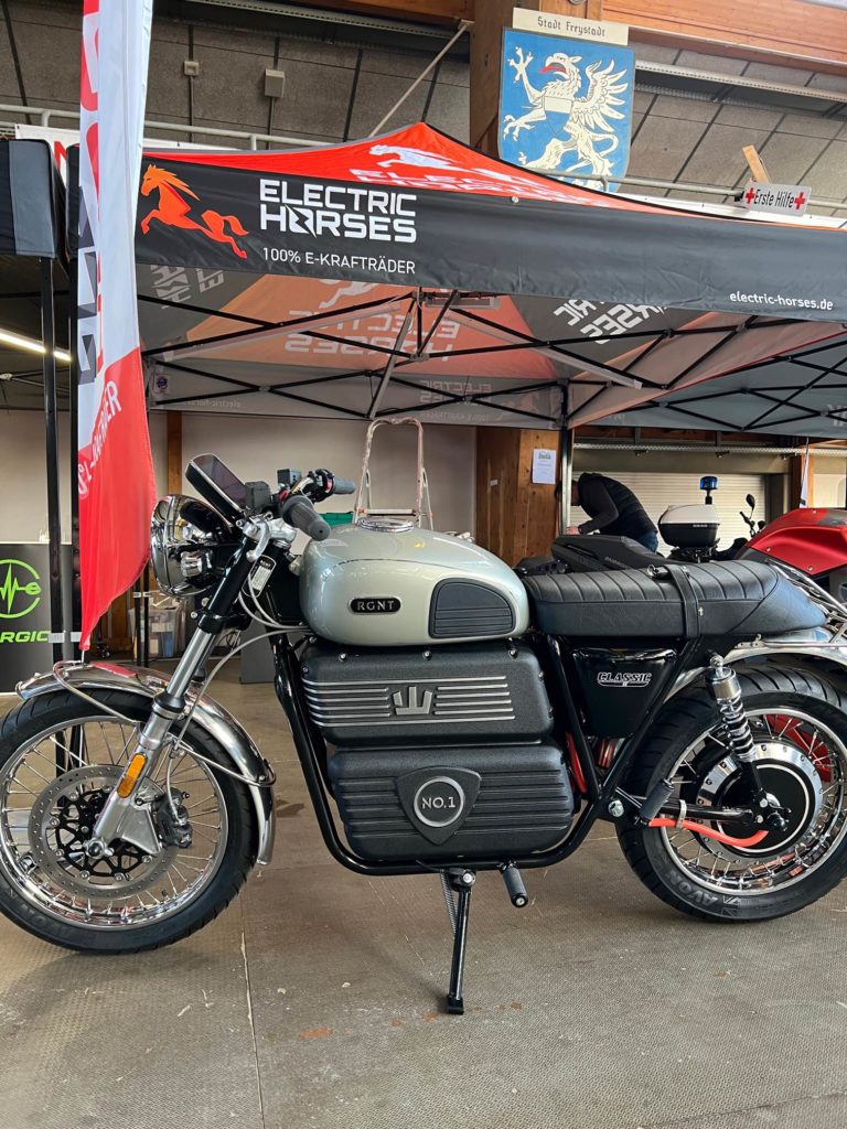 RGNT E-Motorrad "Classic" auf der Jura-Bike 2023 vor Electric Horses Stand. Retro-Design, silberner Tank, schwarzer Rahmen.