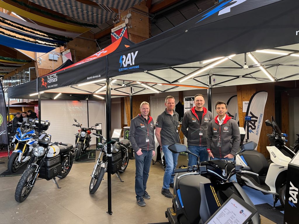 E-Motorräder & E-Roller von Electric Horses auf einer Messe mit 4 Personen vor RAY Zelt.