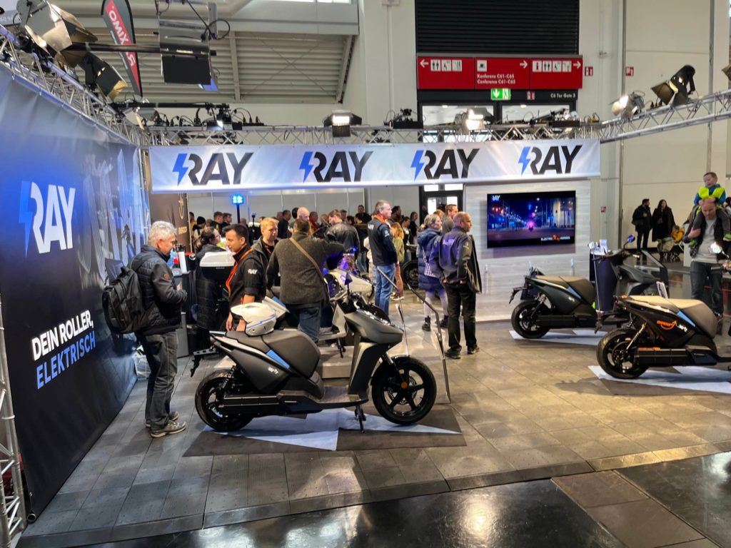 Messestand von Ray auf der IMOT mit E-Rollern und Publikum. Logo: Ray.