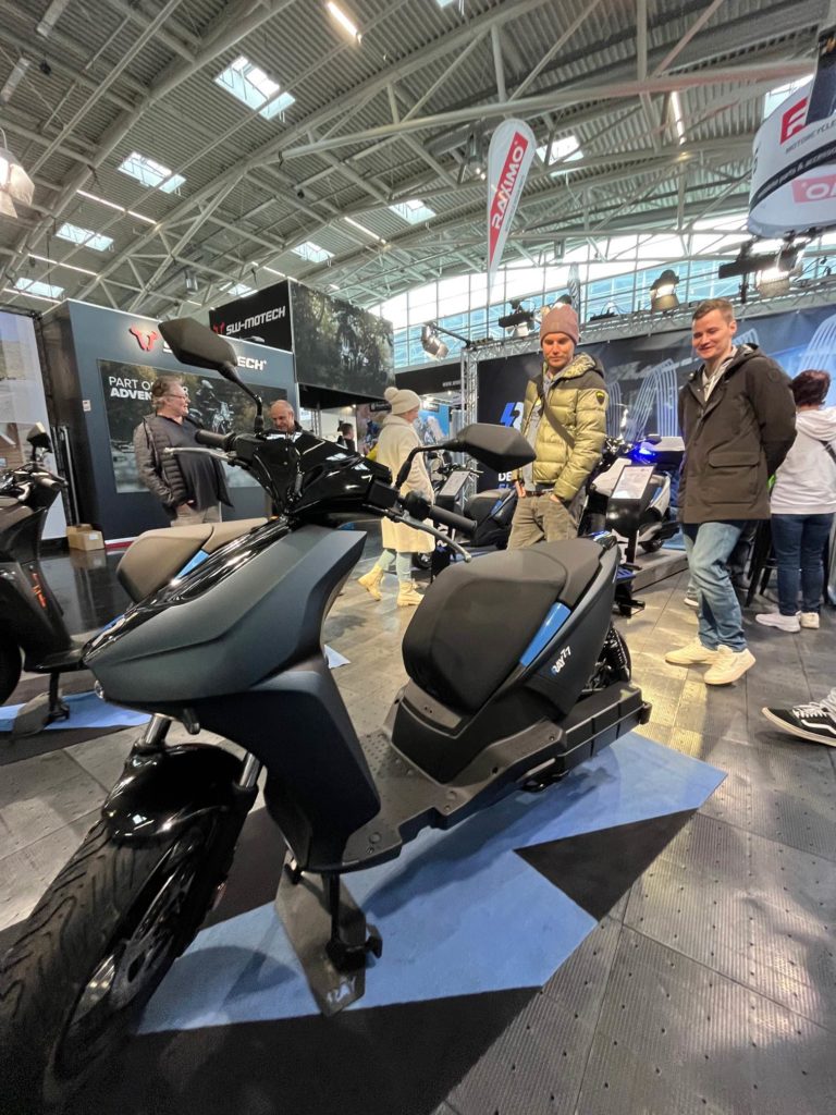E-Roller Ray 7.7 auf der IMOT, Motorrad-Messe. Publikum und Messestand im Hintergrund.