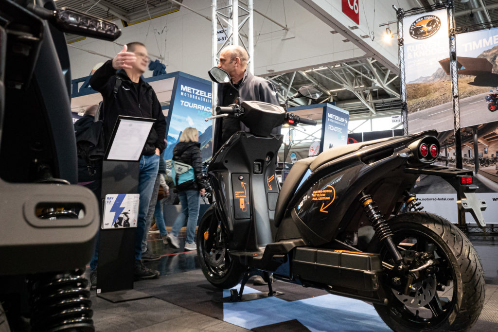 E-Roller RAY 7.7 auf der IMOT Messe. Zwei Männer im Gespräch mit Blick auf das Elektrofahrzeug.